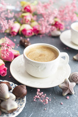 A cup of fragrant coffee in the morning and a bouquet of pink flowers. Chocolate sweets in the form of cockleshells. Shells on the cups. Romance and light colors