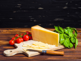 wooden board with parmesan cheese, fresh cherry tomatoes, and green basil. The knife for cutting vegetables. Appetizing still life from vegetables