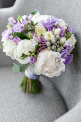 Brides wedding bouquet with peonies, freesia and other flowers on black arm chair. Light and lilac spring color. Morning in room