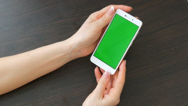 Female hands with beautiful French manicure take a white smartphone with Green Screen. Using Smartphone,Holding Smartphone with Green Screen