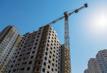 Fototapeta na wymiar Yellow crane and high building construction site against blue sky