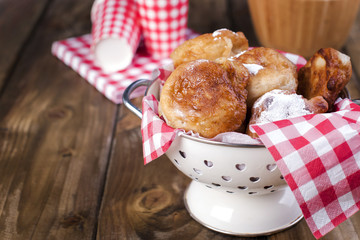 Homemade fried balls with powdered sugar. Napkin in red cage and glass. Brown wooden background. Traditional Baking Netherlands