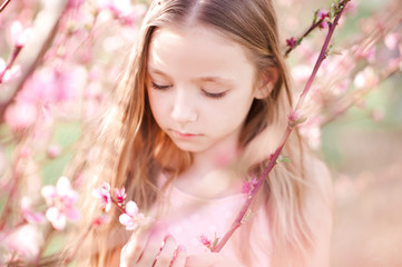 Fototapeta premium Cute kid girl 3-4 year old posing over peach tree outdoors. Spring portrait. Childhood.