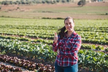 young technical woman smiling and looking to the camera with thumb up in a field of lettuces