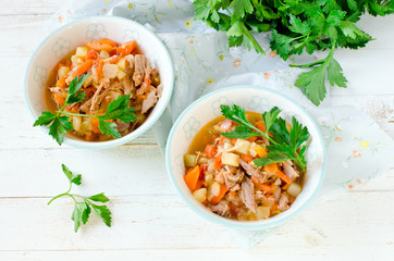 Stew of turkey and vegetables (zucchini, onions, carrots, tomatoes, bell peppers) on a white wooden table
