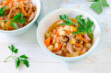 Stew of turkey and vegetables (zucchini, onions, carrots, tomatoes, bell peppers) on a white wooden table