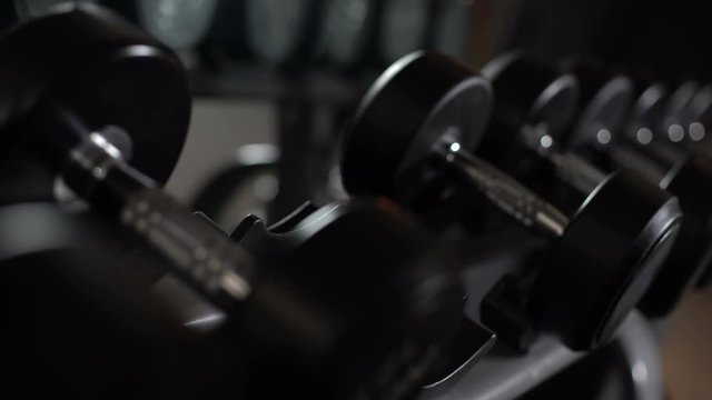 Closeup of male hand taking dumbbells, strength training equipment in gym
