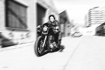 Naklejka premium Modern biker speeds up motorcycle on a industrial street. Outdoor portrait and urban lifestyle