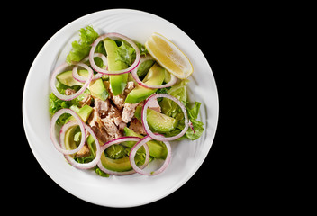Tuna salad with avocado and arugula on a white plate, on a black background.