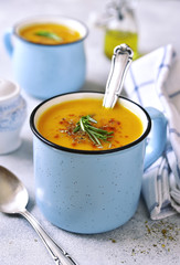 Two portions of pumpkin creamy soup in a blue emamel mugs.