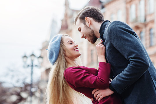Outdoor portrait of young beautiful happy smiling couple posing in street of the old european city. Models embrace and look at each other. Copy, empty space for text