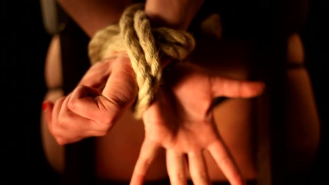 girl has hands bound behind their backs with rope