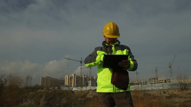 mature male worker foreman in helmet with a tablet on the background of construction