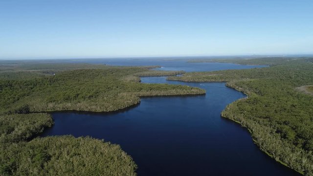 High over blue clean waters of Myall lakes and streams between evergreen woods with fishing boats and recreational opportunities in national park of Australia.
