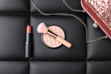 Makeup products, brush and handbag on black leather background