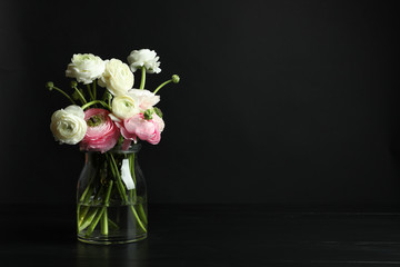 Glass vase with beautiful ranunculus flowers on black background