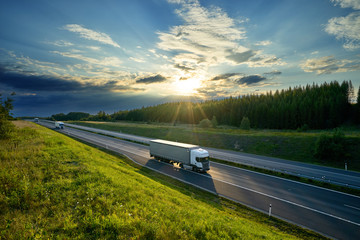 White trucks driving on the highway in the countryside in the rays of the sunset with dramatic clouds