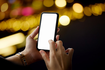 Woman holding mobile phone over night bokeh blurred background.