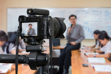 Fototapeta na wymiar Professional digital Mirrorless camera on the tripod recording video blog of Asian teacher in the classroom,Camera for photographer or Video and Technology Live Streaming concept,University education