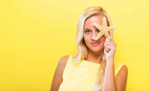 Happy young woman holding a starfish on a solid background