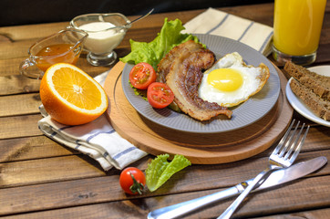 English Breakfast: fried egg with bacon, orange juice, tomatoes, zernovoi bread, lettuce leaf, top view.