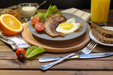 English Breakfast: fried egg with bacon, orange juice, tomatoes, zernovoi bread, lettuce leaf, top view.