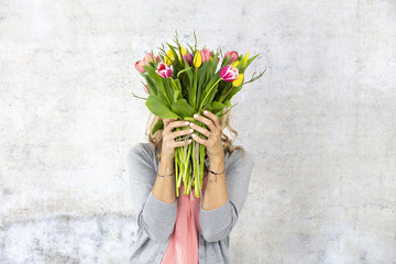 Young pretty woman with a bouquet of flowers stands in front of concrete wall and is happy about mother's day, birthday, wedding day