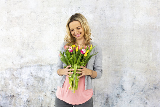 Young pretty woman with a bouquet of flowers stands in front of concrete wall and is happy about mother's day, birthday, wedding day