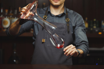 Sommelier pouring wine into glass from mixing bowl. Male waiter