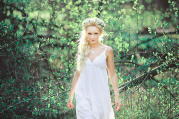 Naklejka premium beautiful woman in white dress and floral wreath on her head among the blossoming leaves.