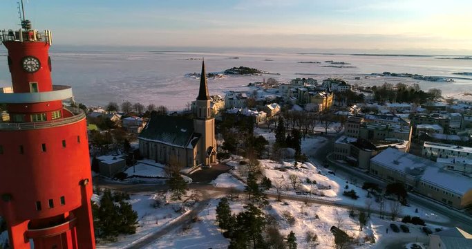 Frozen city, Cinema 4k aerial view around a water tower and revealing a church, in a icy Hanko cityscape, on a cold sunny winter evening dawn, in Uusimaa, Finland