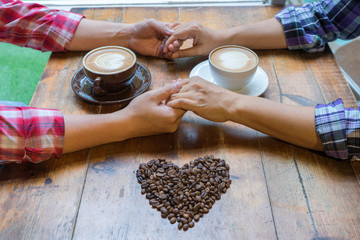 Couple in love holding hands with coffee on  wooden table. Photograph taken from above, side view with heart coffee