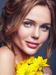 Beauty fashion portrait of young blond woman model with natural makeup and perfect skin with bright yellow chrysanthemum flower posing in studio