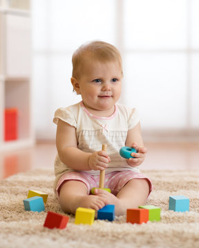 Little baby toddler playing with colorful toy pyramid sitting on floor in white sunny bedroom. Toys for little kids. Child with educational toys. Early development.