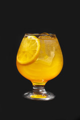 Single-colored cocktail, yellow refreshing in low plump glass with ice cubes and a round slice of orange, lemon with the taste of pineapple, melon, peach, apricot. Side view Isolated black background