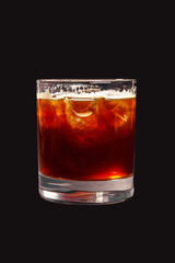 Single-colored transparent cocktail, brown, red refreshing carbonated with foam in a low glass with ice cubes and cola taste. Side view. Isolated black background. Drink for the menu