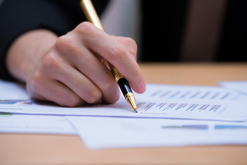 Working desk with people sitting. Hand right of businessman holding a pen and writing graphs paper.