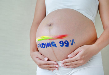 Pregnant woman with word loading 99%. Concept painted on pregnancy tummy.