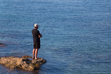 Fototapeta na wymiar A man catches fish. Standing on a rock in the water.