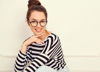 Portrait of young beautiful brunette woman girl model with nude makeup in glasses in summer hipster clothes posing near wall. Sitting on the floor