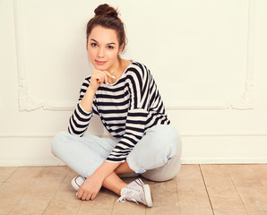 Portrait of young beautiful brunette woman girl model with nude makeup in summer hipster clothes posing near wall. Sitting on the floor