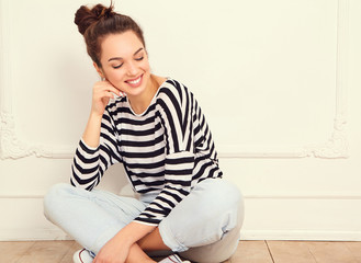 Fototapeta premium Portrait of young beautiful brunette woman girl model with nude makeup in summer hipster clothes posing near wall. Sitting on the floor