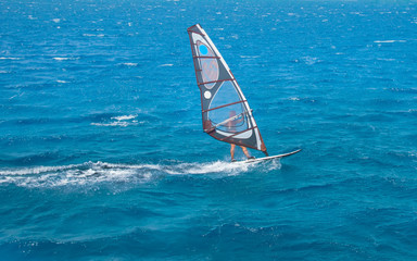 the windsurfer on the board under sail moves at a speed along the surface of the sea