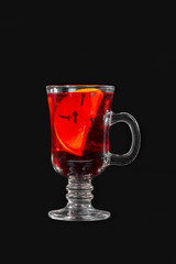 Monochrome transparent cocktail, red mulled wine in a high glass with a handle with spices and a slice of lemon, orange. Side view. Isolated black background. Drink for the menu restaurant, bar, cafe