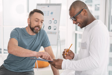 Fototapeta premium What is it. Nice pleasant man pointing at the notes while asking questions to the doctor