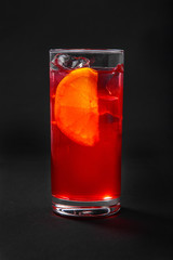 A single-colored transparent cocktail, refreshing in a tall glass with ice cubes, orange slice, lemon and taste of berries, cherries, strawberries, greiprut. Side view. Isolated black background