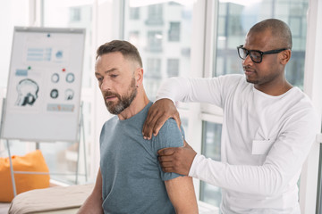 Physical therapy. Smart nice man touching his patients shoulder while doing the therapy