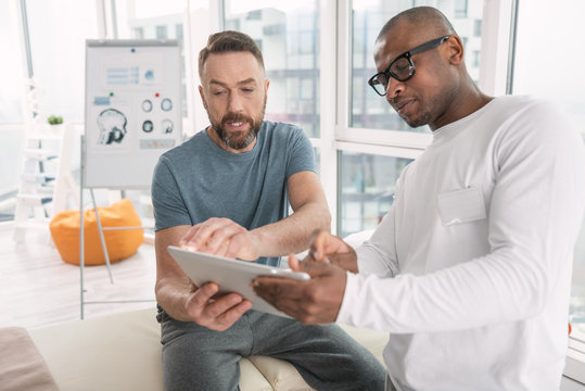 Modern Device. Serious Nice Bearded Man Looking At The Tablet Screen While Talking To His Doctor