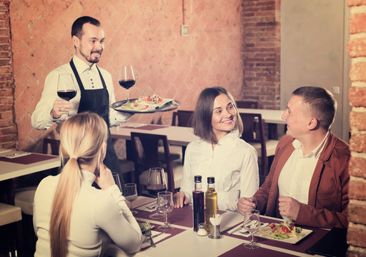 Young waiter placing order in front of guests