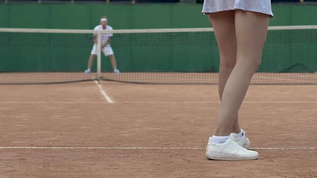 Young sport lady bouncing tennis ball for serving, starting match, back view